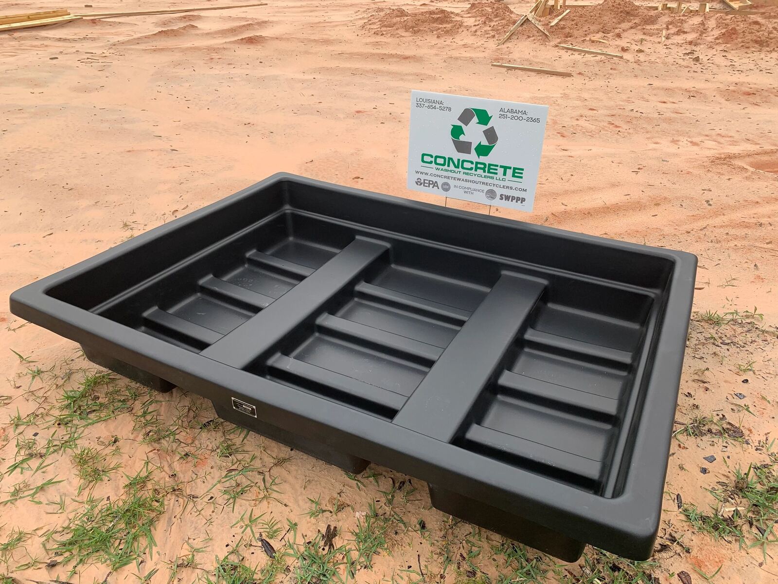 A reusable concrete washout basin set on a job site, with the Concrete Washout Recyclers sign behind it